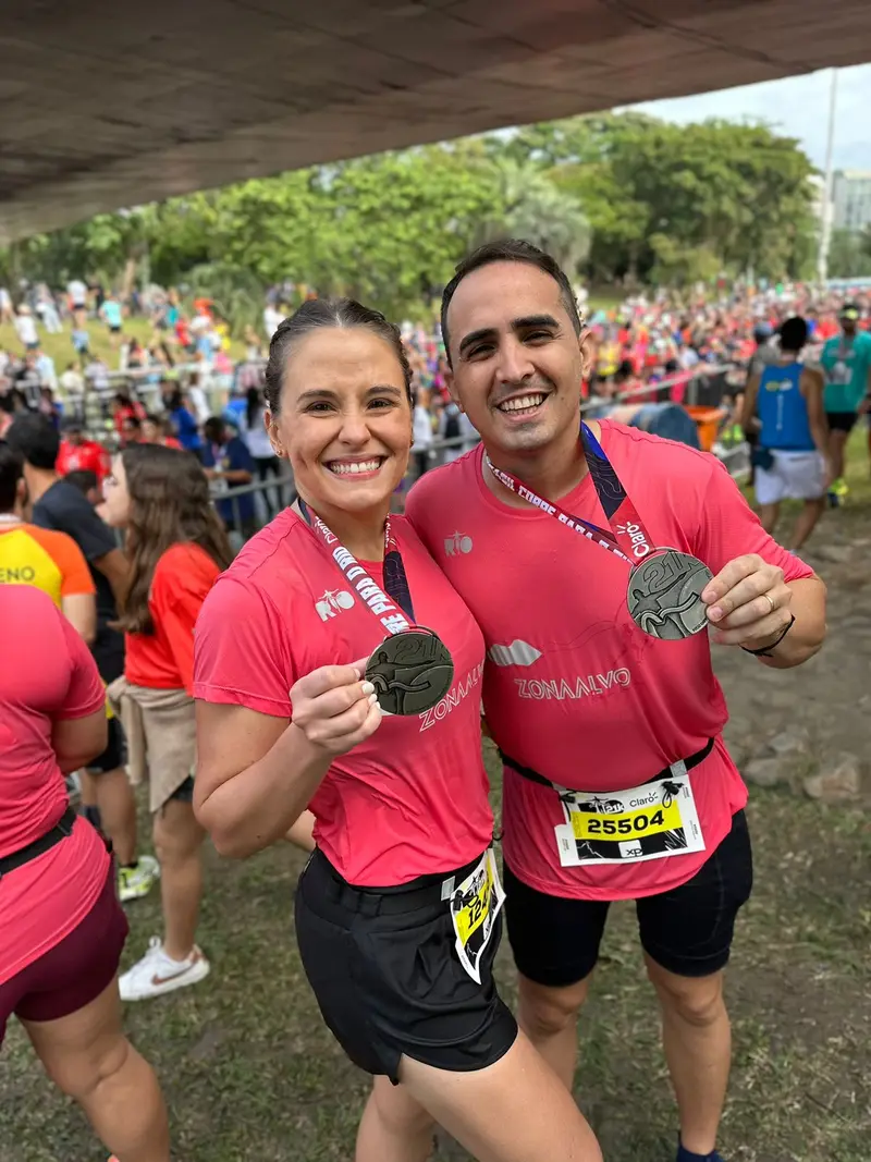 Casal de corredores com camisetas rosa exibindo as medalhas